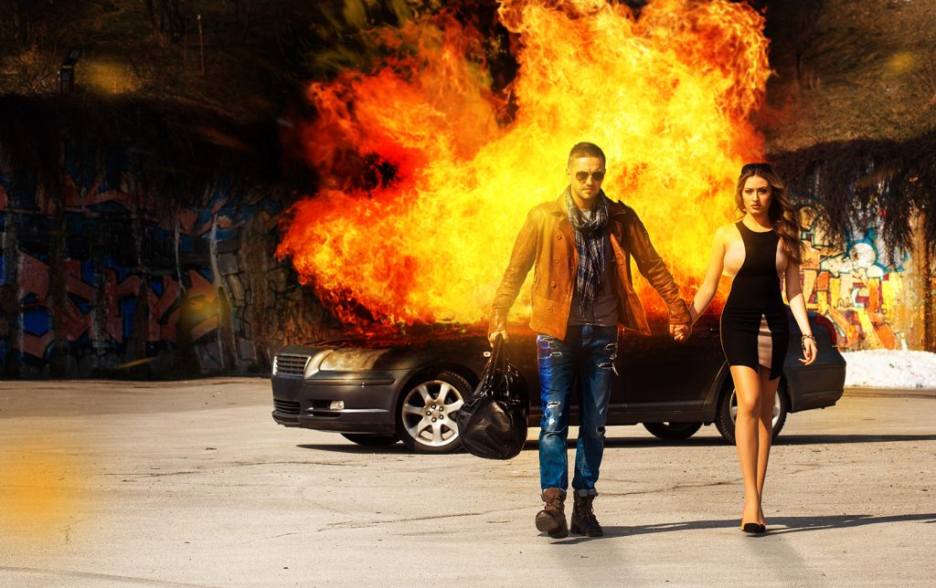 Horizontal picture of the blockbuster as a man and a woman go away from burning car outdoors