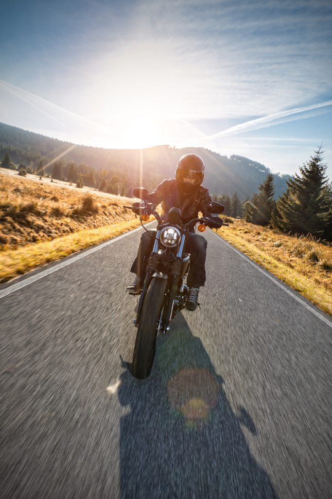 Motorcycle driver riding on motorway in beautiful sunset light. Shot from front view