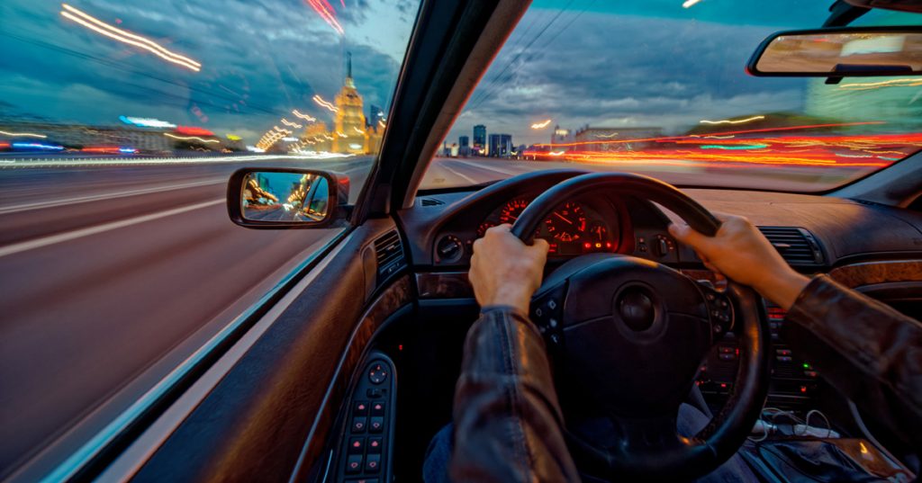 Movement of the car at night at high speed view from the interior with driver hands on wheel. Concept spped of life. Long exposure photo.