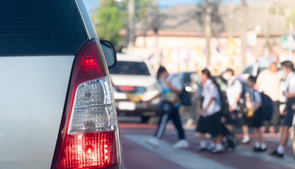 Rear side of car with turn on brake light on the road. Road crossing point with blurry image of students passing by.  Many cars had to stop to pass for safety reasons. Morning time in the city.